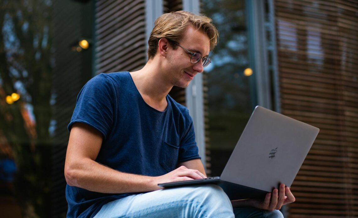 A young man sitting outdoors in Leiden, Netherlands, working on a laptop.